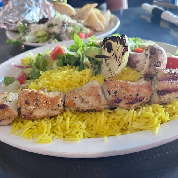 Chicken shish kebab with yellow rice, salad, and grilled vegetables on a white plate.