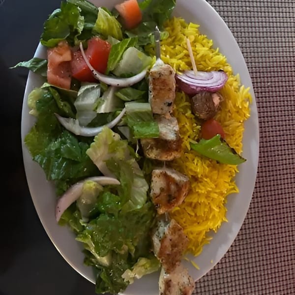 Chicken shish kebab with yellow rice and a fresh green salad with tomatoes and onions.