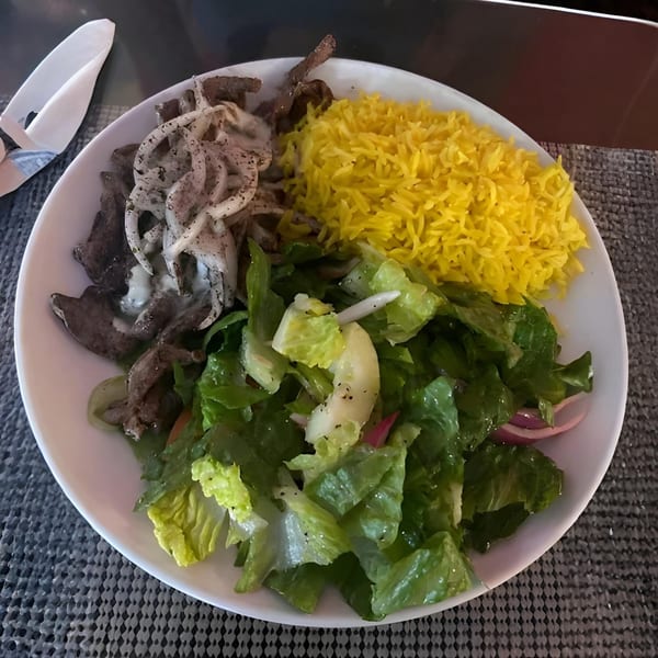 A Mediterranean dish with sliced meat, white onions, yellow rice, and a green salad on a white plate.